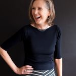 A photo of Mary Roach laughing at something to the left of the camera, with her hand on her hip.